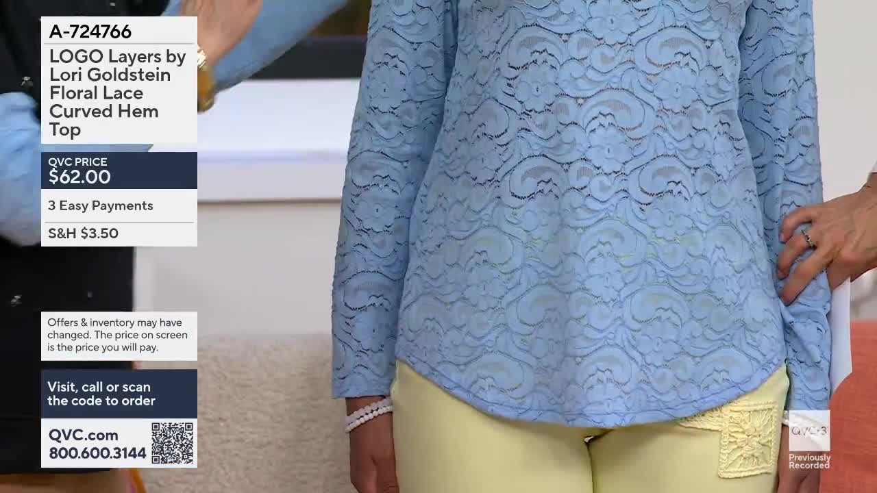 A woman models a light blue lace top over yellow pants. Another person's hand adjusts the fabric on the side of the top.