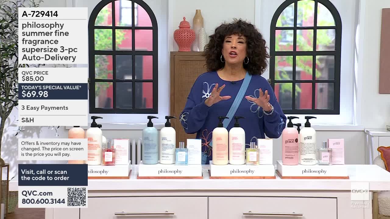 A woman gestures enthusiastically in front of a display of Philosophy brand body care products. Bottles of lotion and fragrance are neatly arranged on white stands.