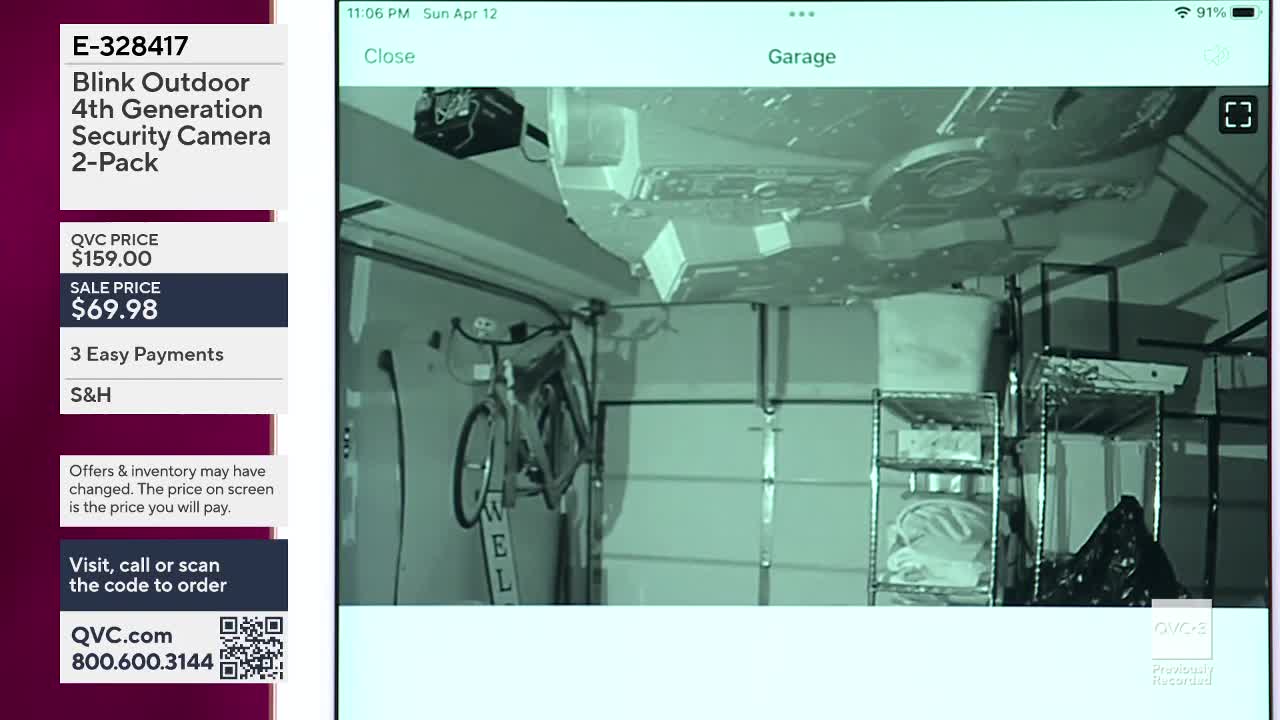 A bicycle hangs from the wall in a garage, illuminated by a security camera. Shelving units and a large white bin are visible on the right side.