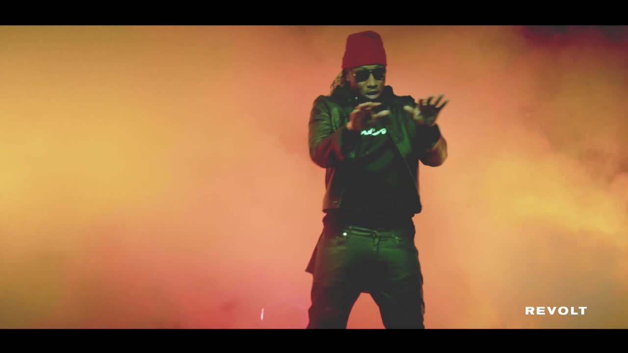Future, in a red beanie and sunglasses, gestures with his hands as he performs. The background is a hazy blend of orange and yellow, with the Revolt logo visible in the bottom right corner.
