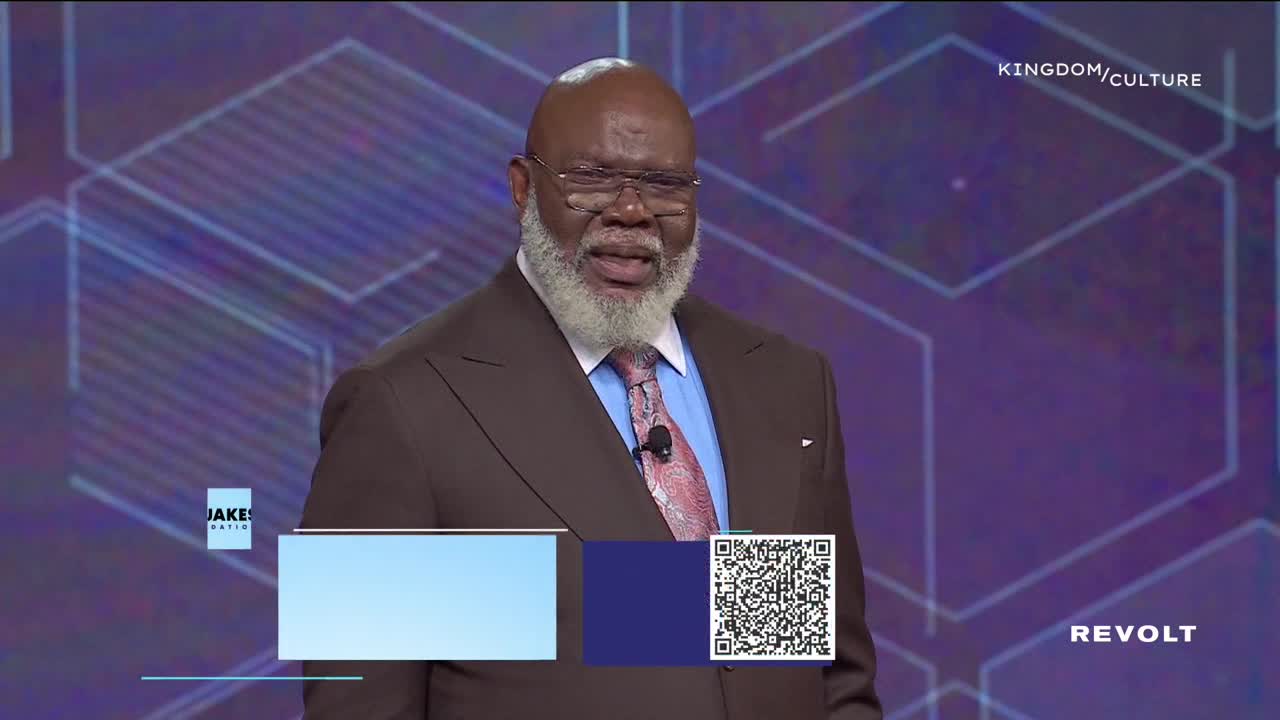 A man in a brown suit and tie is speaking, his expression earnest as he looks toward the audience. Beneath him, a QR code and a "REVOLT" logo are visible on the screen.

