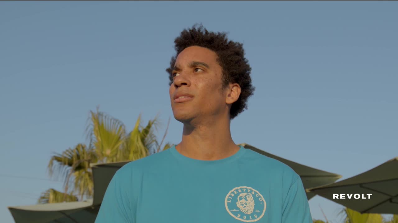 A man in a turquoise t-shirt looks off to the side, his gaze fixed on something unseen. The logo on his shirt reads "Libertango," and the word "Revolt" is visible in the corner.
