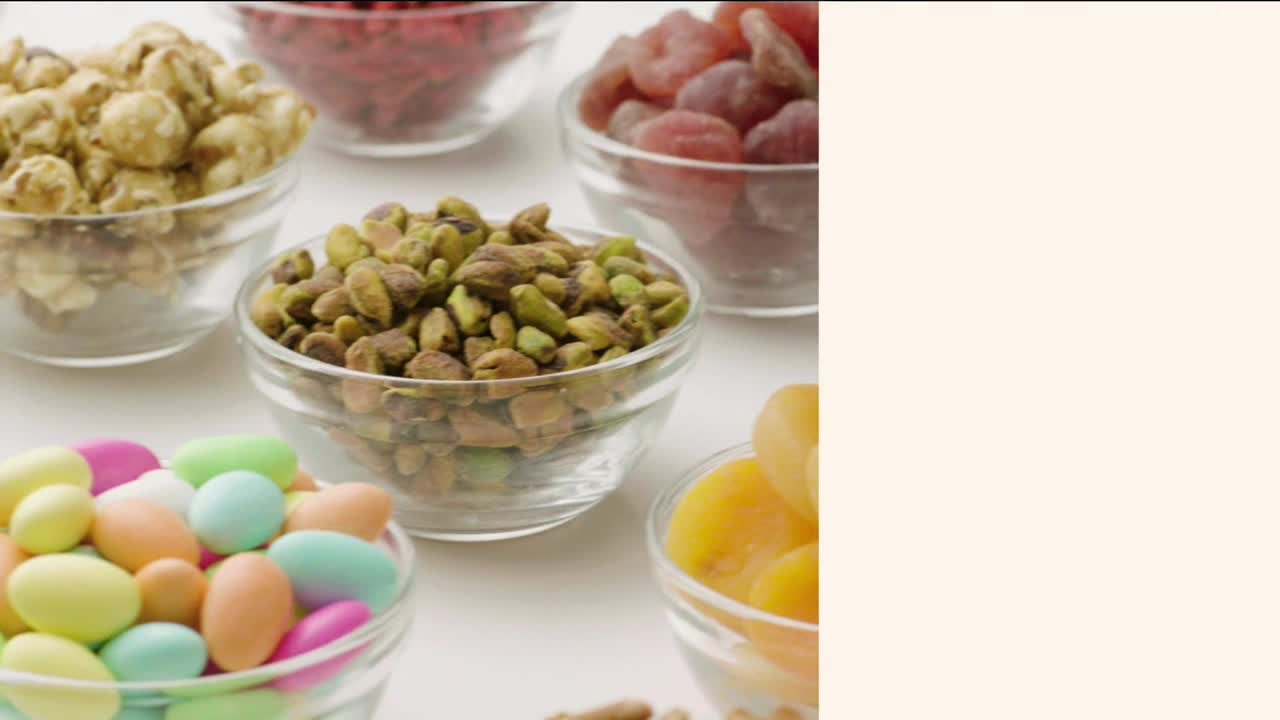 A variety of treats, from pistachios to sugared almonds, are arranged in small glass bowls. The bowls are set on a white surface, and the composition is well-lit.
