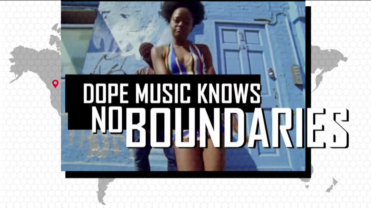 A woman in a colorful swimsuit stands in front of a blue door, a man partially visible behind her. The words "DOPE MUSIC KNOWS NO BOUNDARIES" are superimposed over the scene.
