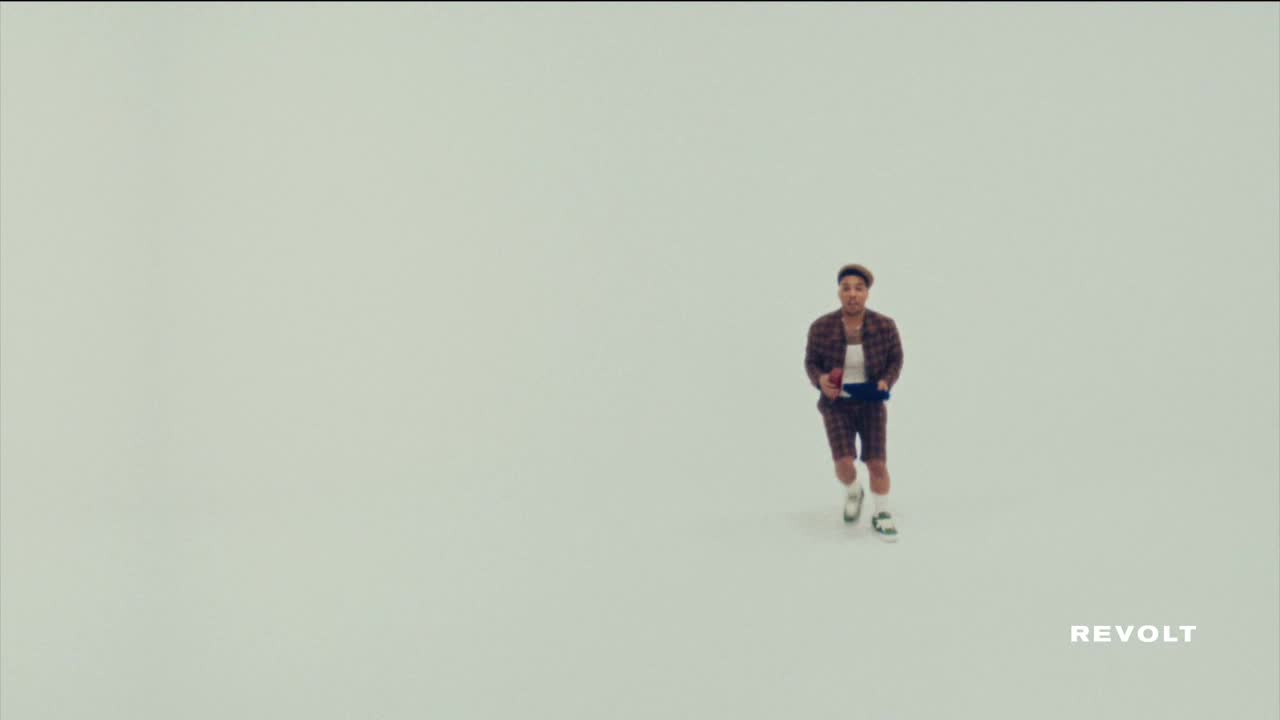 A person in a plaid outfit jogs across a vast, empty space, holding something in their hands. The Revolt logo is visible in the corner.

