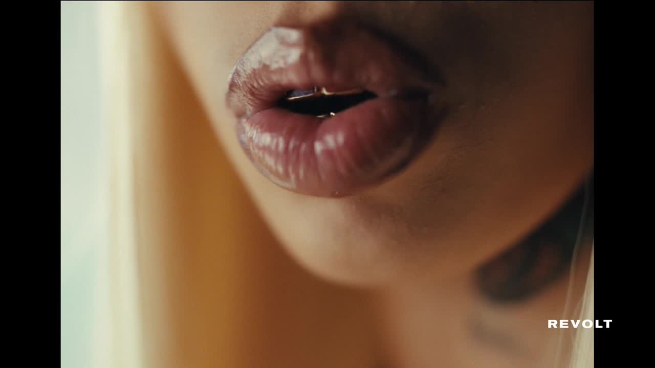 Glossy, full lips are slightly parted, reflecting the light. The word "REVOLT" is visible in the bottom right corner.

