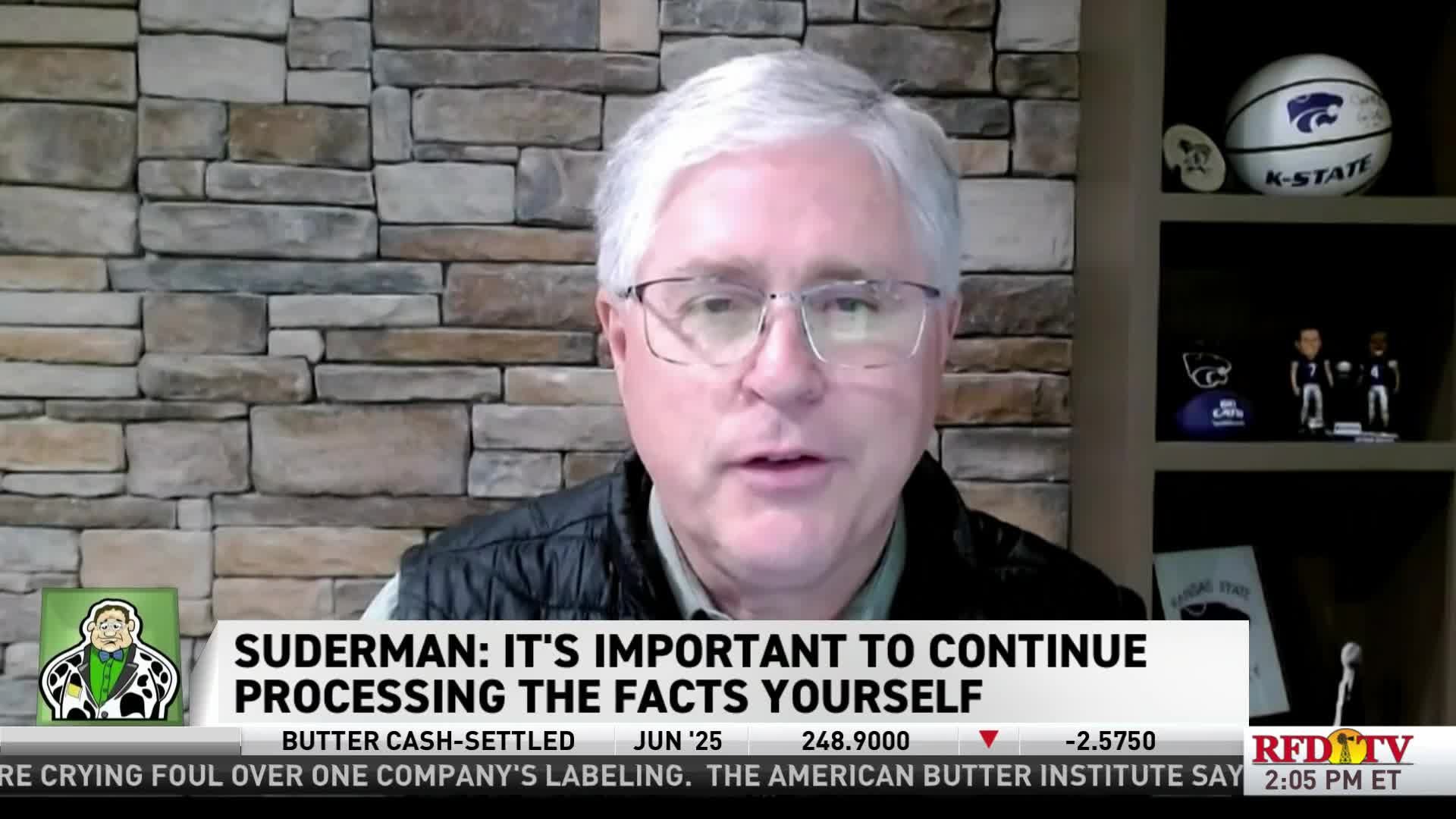 On RFD-TV, a man in glasses is speaking, the chyron below him emphasizing the importance of independent fact-checking. Behind him, a shelf displays a K-State basketball and bobbleheads.
