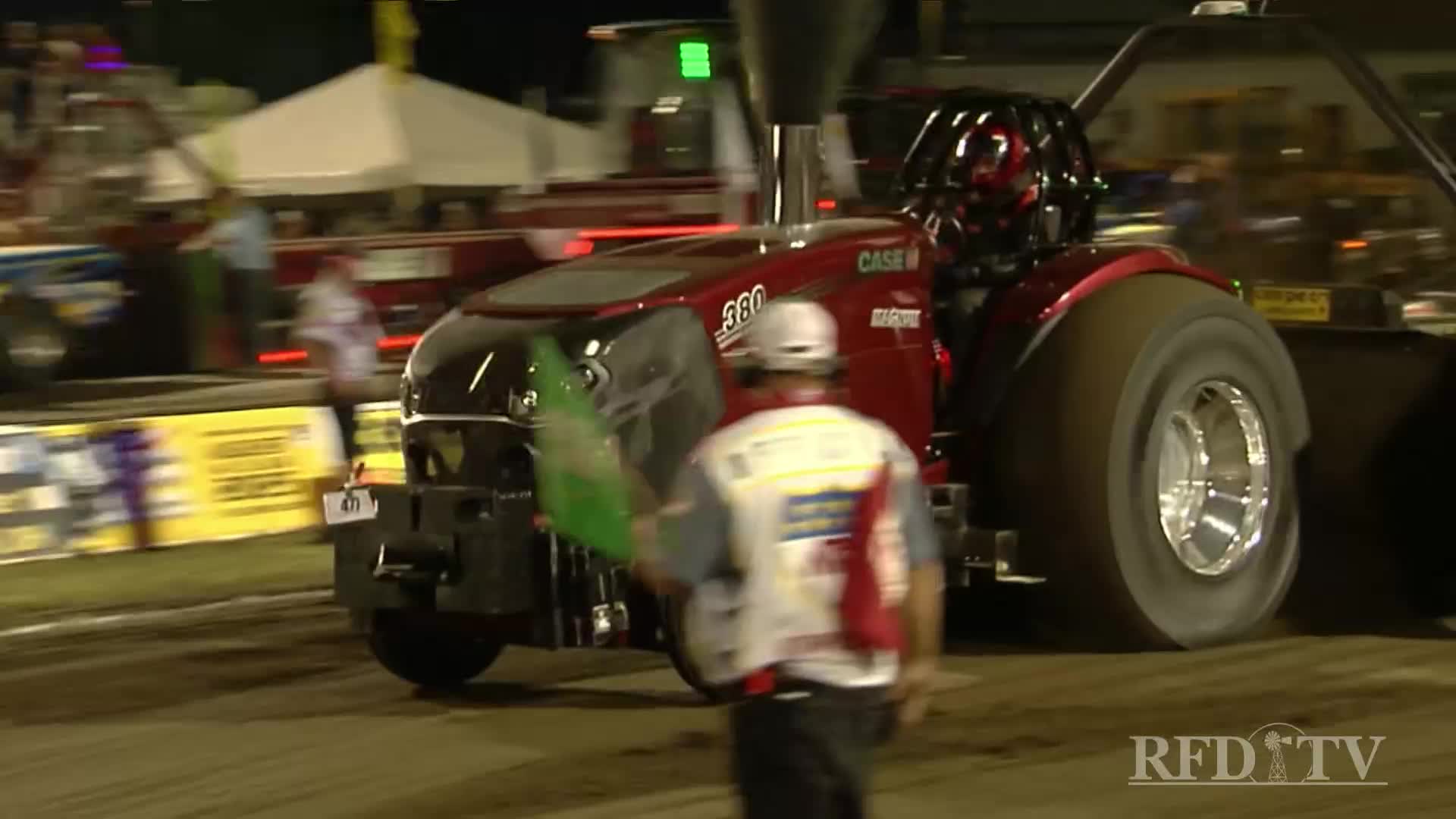 The Case IH tractor is roaring, its massive rear tires spinning as it pulls. A track official waves the green flag, signaling the start of the pull.

