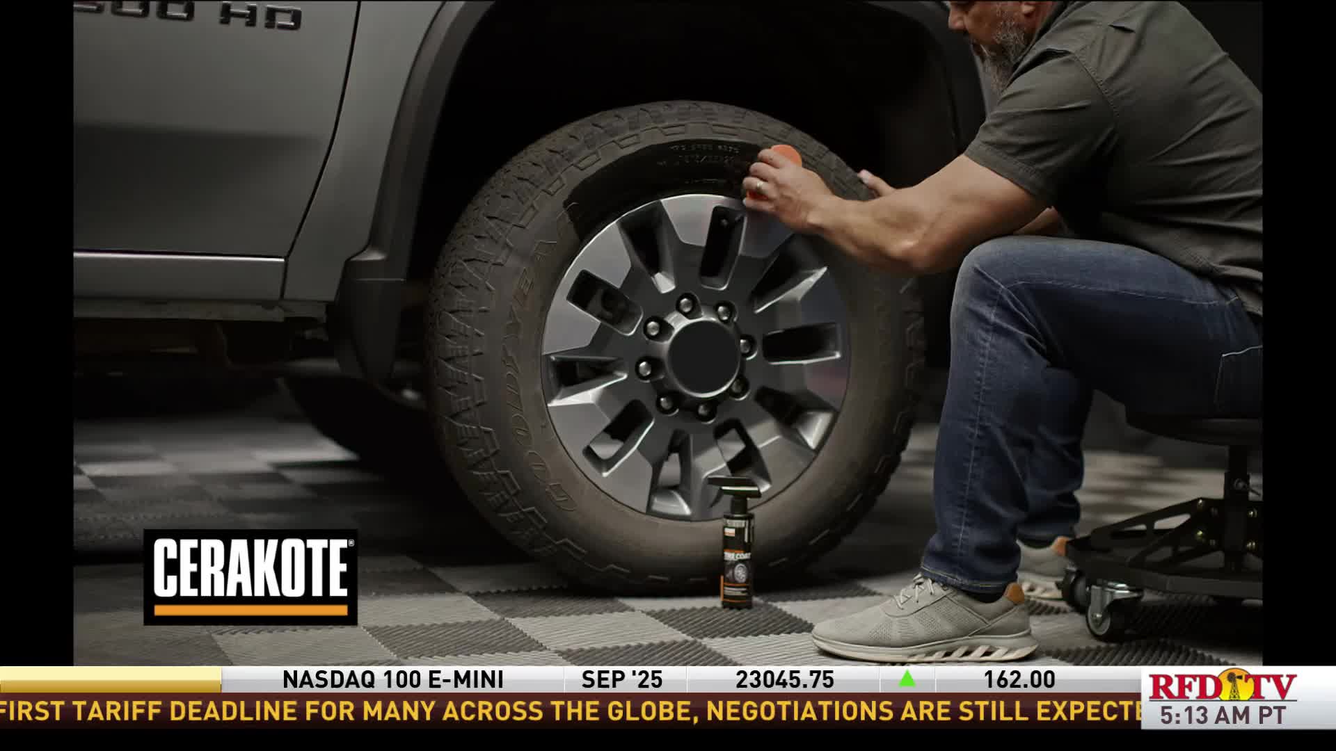 A man is seated, applying a product to a truck tire with a small orange applicator. The RFD-TV ticker at the bottom of the screen reports on global trade negotiations.
