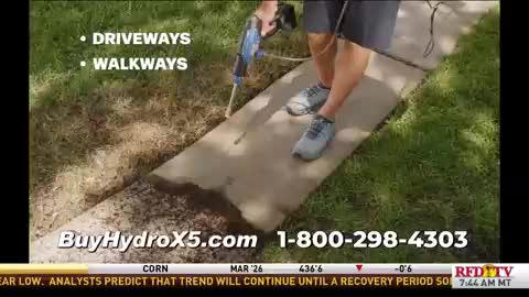 A man is spraying a concrete walkway with a blue power washer, and the dirty surface is visibly cleaning up. The demonstration is likely from a commercial on RFD-TV, as the website and phone number are displayed at the bottom.
