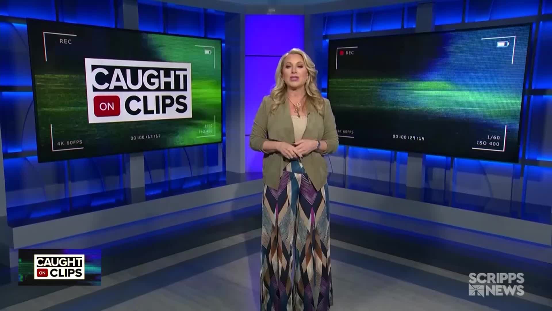 A woman in a blazer and patterned pants stands in a studio, facing the camera. Behind her, two screens display the "Caught on Clips" logo, with a Scripps News logo visible in the corner.
