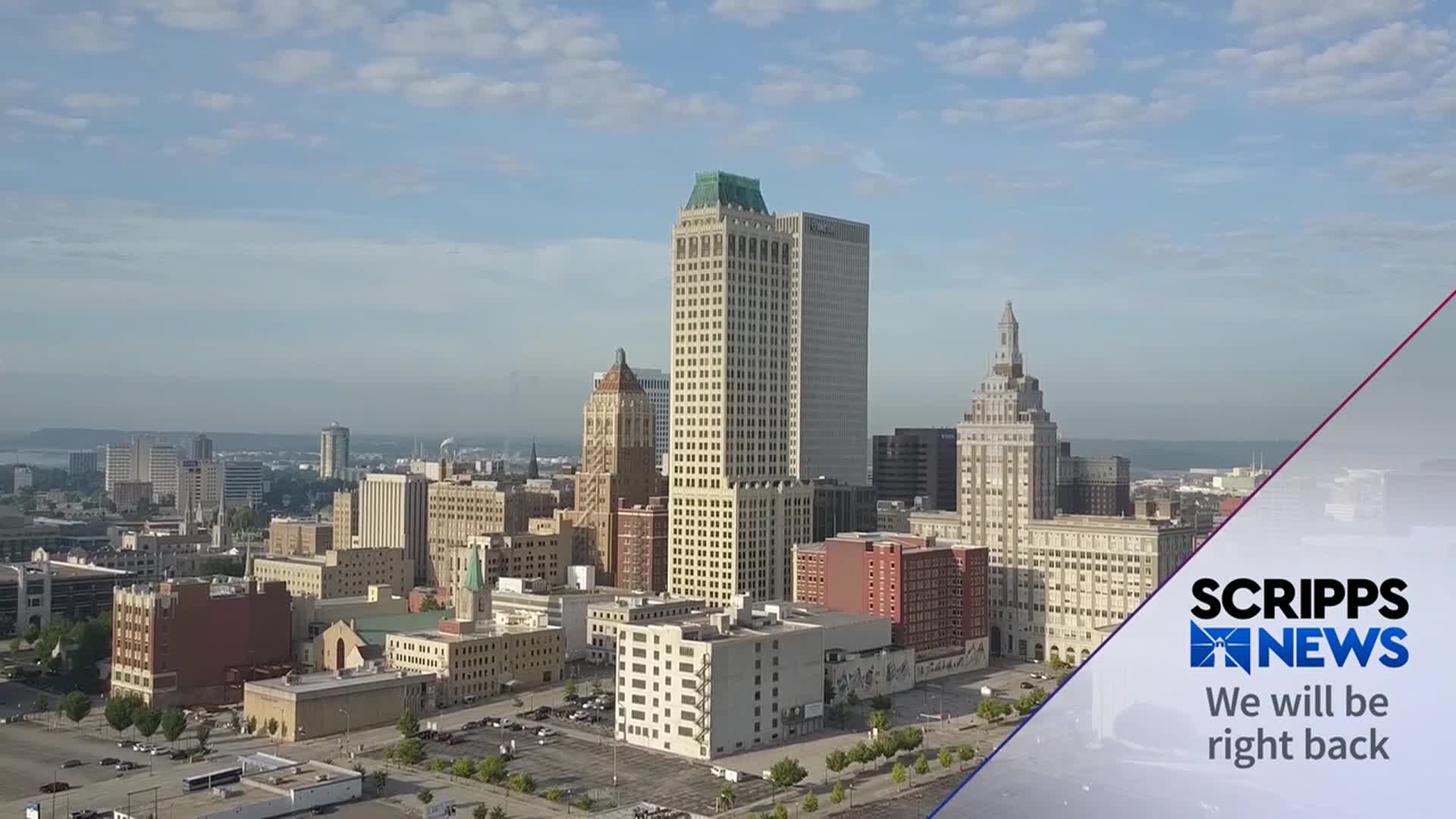Sunlight bathes the downtown skyline of a United States city, as seen on Scripps News. The camera angle looks down on the buildings, with a clear view of the city's architecture.
