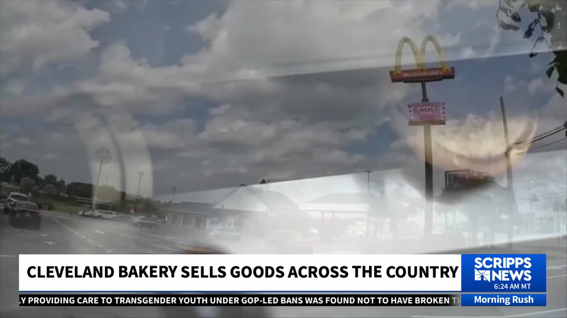 A McDonald's sign stands tall against a cloudy sky, visible through a layered image from Scripps News. Cars travel on a nearby road, and the lower third of the screen displays a news headline about a Cleveland bakery.
