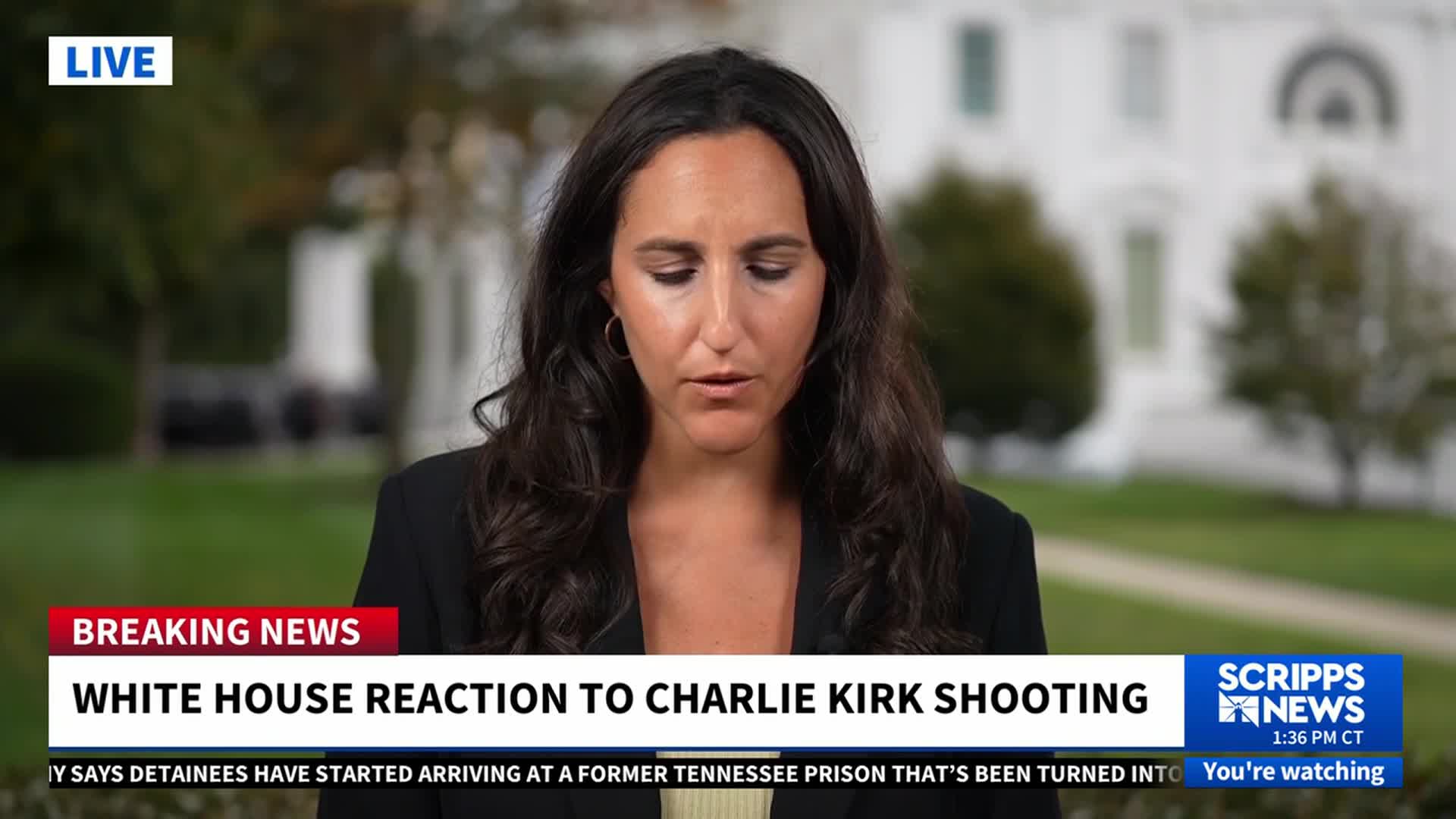 A Scripps News reporter is speaking, her gaze fixed downward as she delivers live coverage. Behind her, the White House is visible, framed by a lush green lawn.
