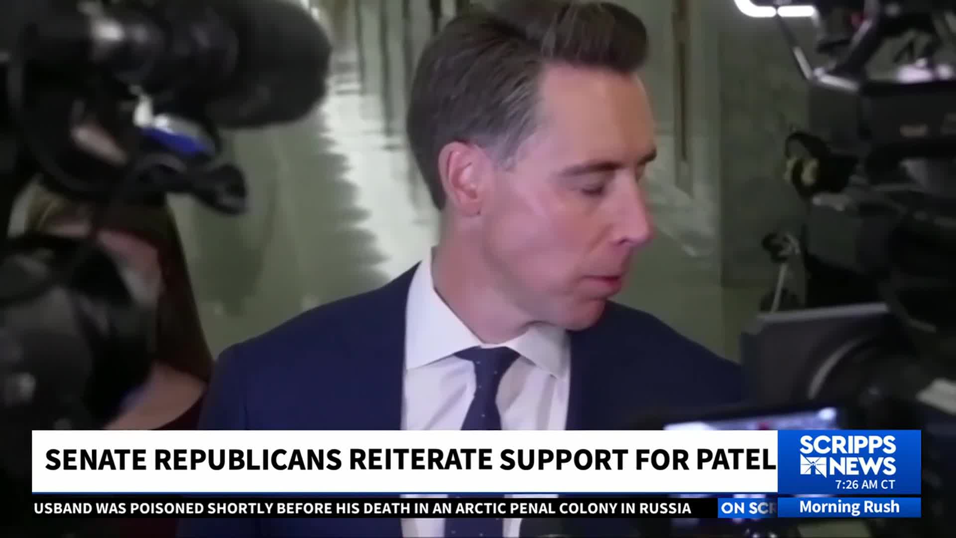 A man in a suit, likely a reporter, is walking and looking down, surrounded by cameras and equipment.  Scripps News graphics are visible at the bottom of the frame, and the headline reads "Senate Republicans Reiterate Support for Patel."
