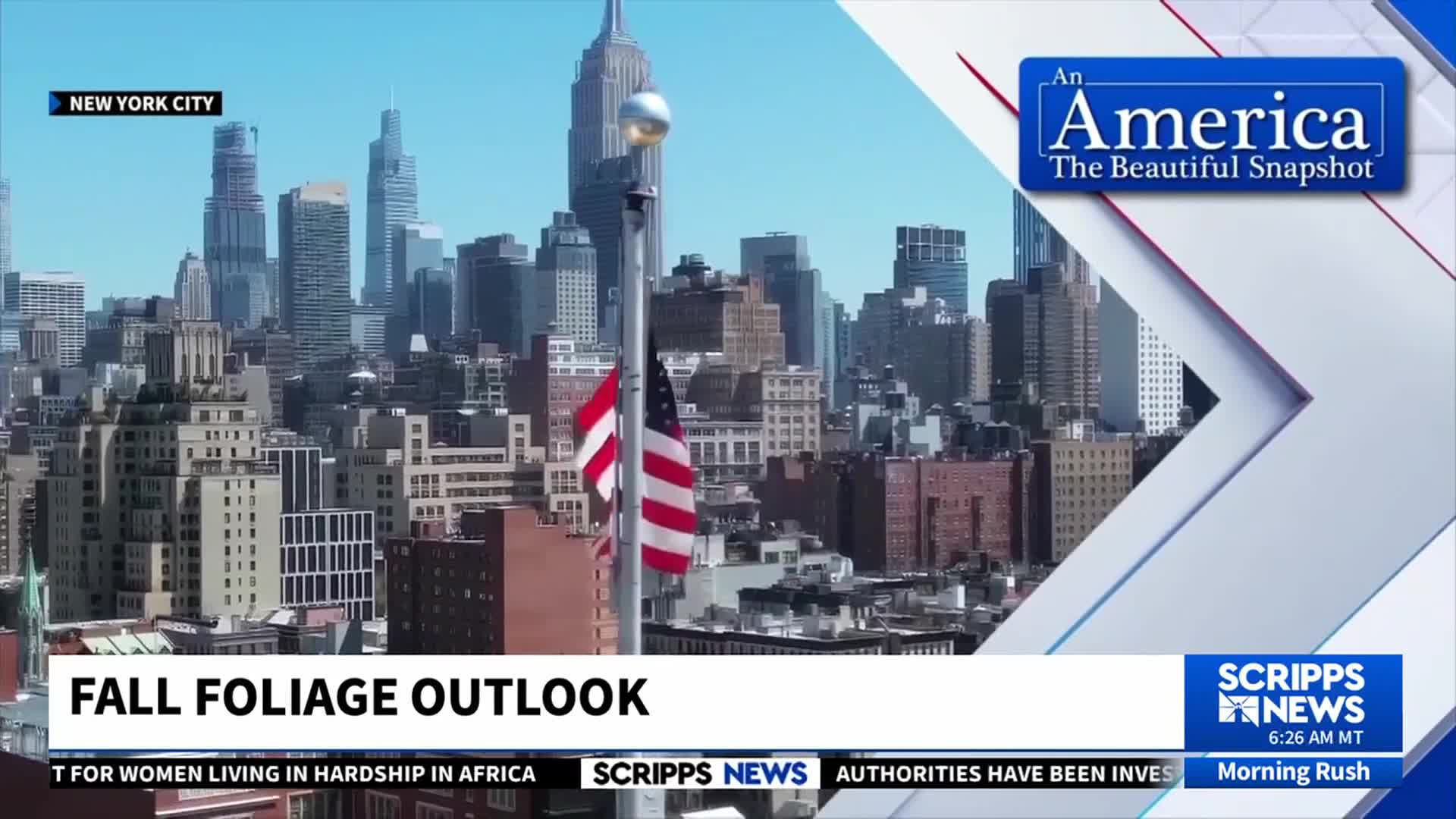The American flag and another, smaller flag, both flap in the breeze against a backdrop of New York City skyscrapers. A Scripps News graphic displays information about the fall foliage outlook.
