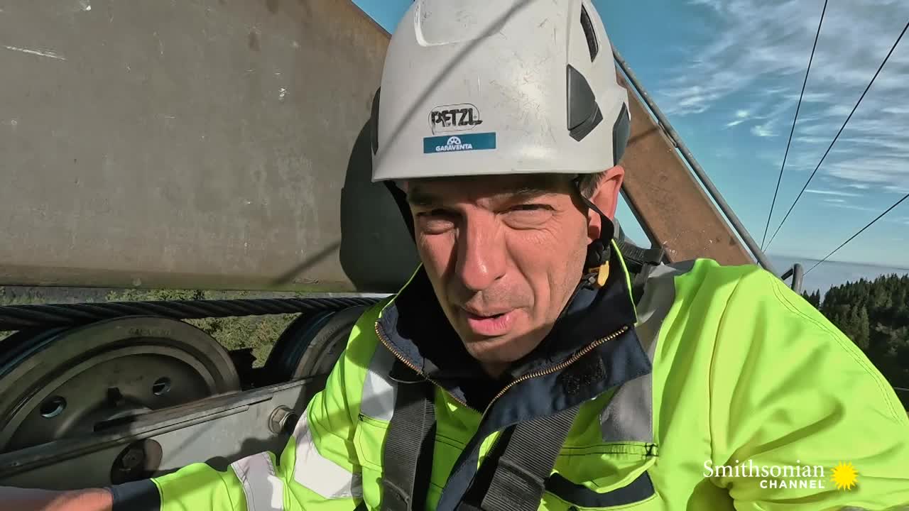 A man in a hard hat and safety gear is positioned next to a large cable and pulley system. The Smithsonian Channel logo is visible, suggesting a documentary setting.

