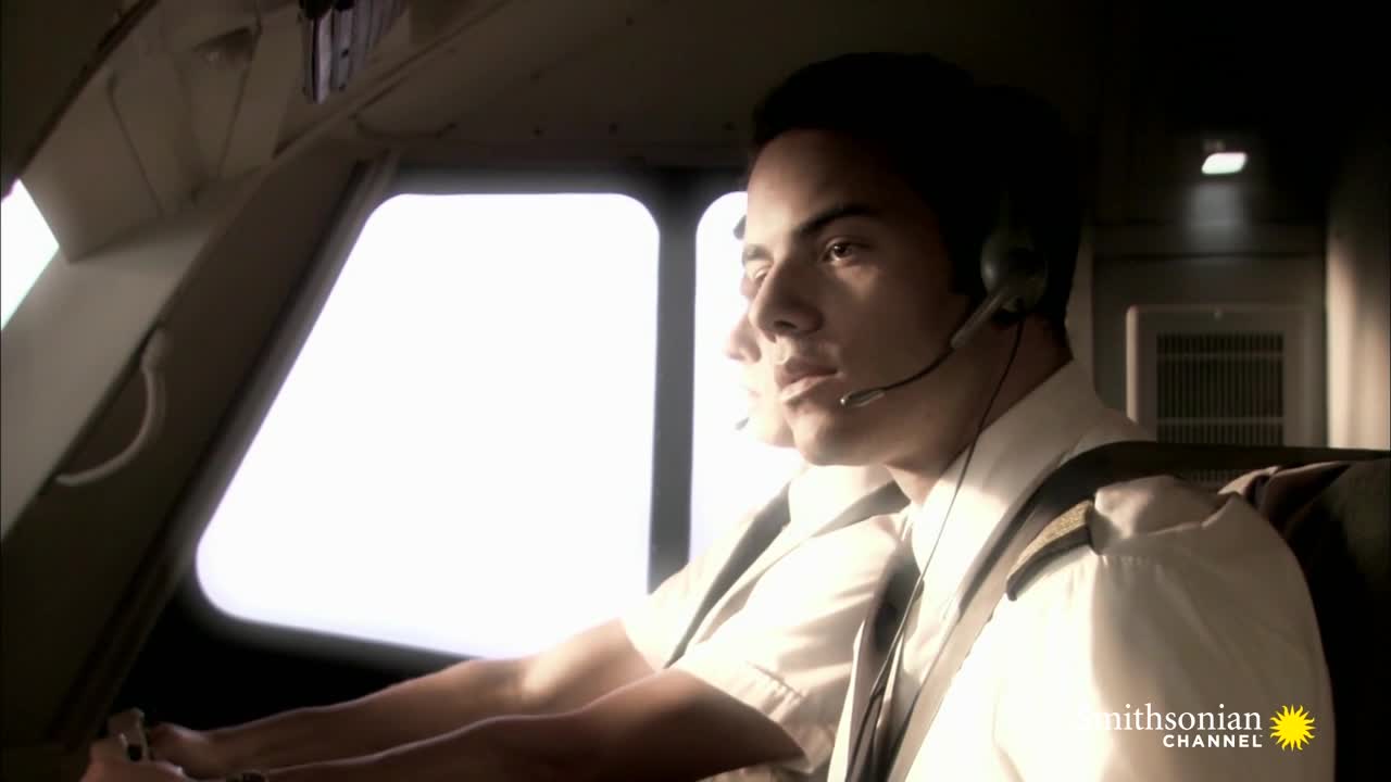 Two pilots, both wearing headsets, sit in the cockpit of an aircraft. Through the bright window, the sky is visible, and the Smithsonian Channel logo is in the corner.
