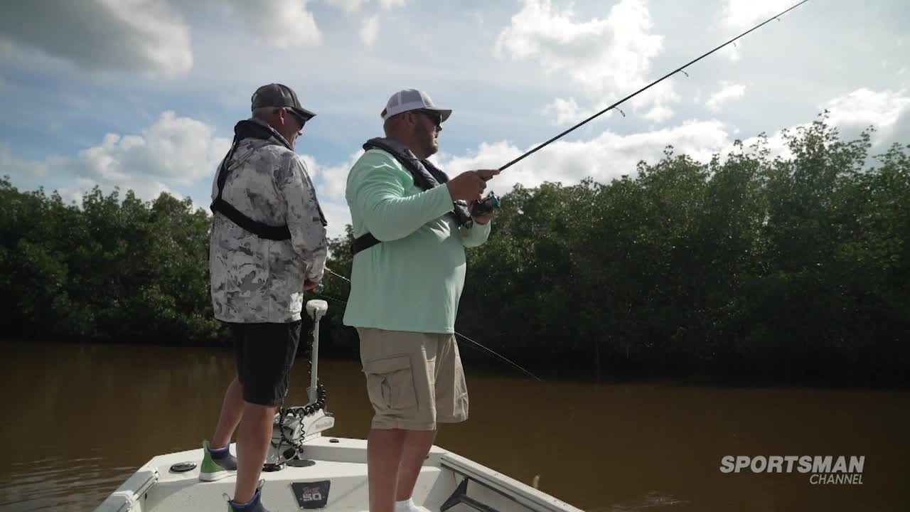 Two men are on a boat, fishing rods in hand, casting lines into the murky water. The Sportsman Channel logo is visible, and the scene suggests a fishing expedition in the United States.
