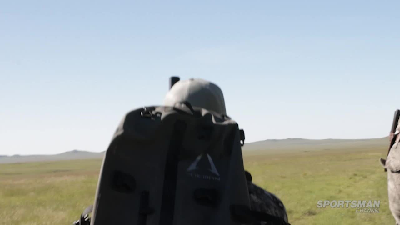 A hunter, viewed from behind, is moving across a vast, grassy plain. The Sportsman Channel logo is visible in the corner, suggesting a program filmed in the United States.
