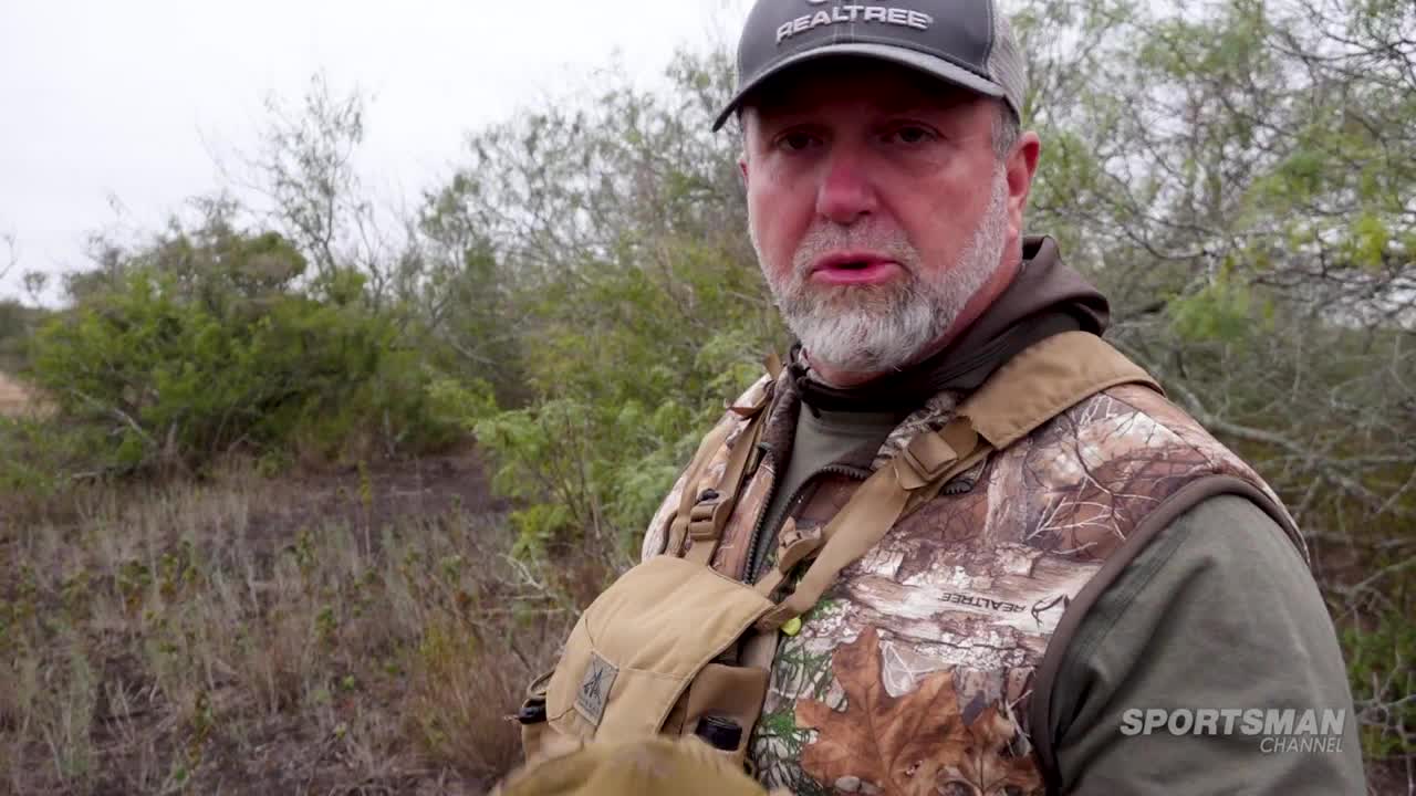 A man in camouflage gear, wearing a Realtree cap, speaks directly to the camera. He's standing in a brushy, overcast landscape, with the Sportsman Channel logo visible.
