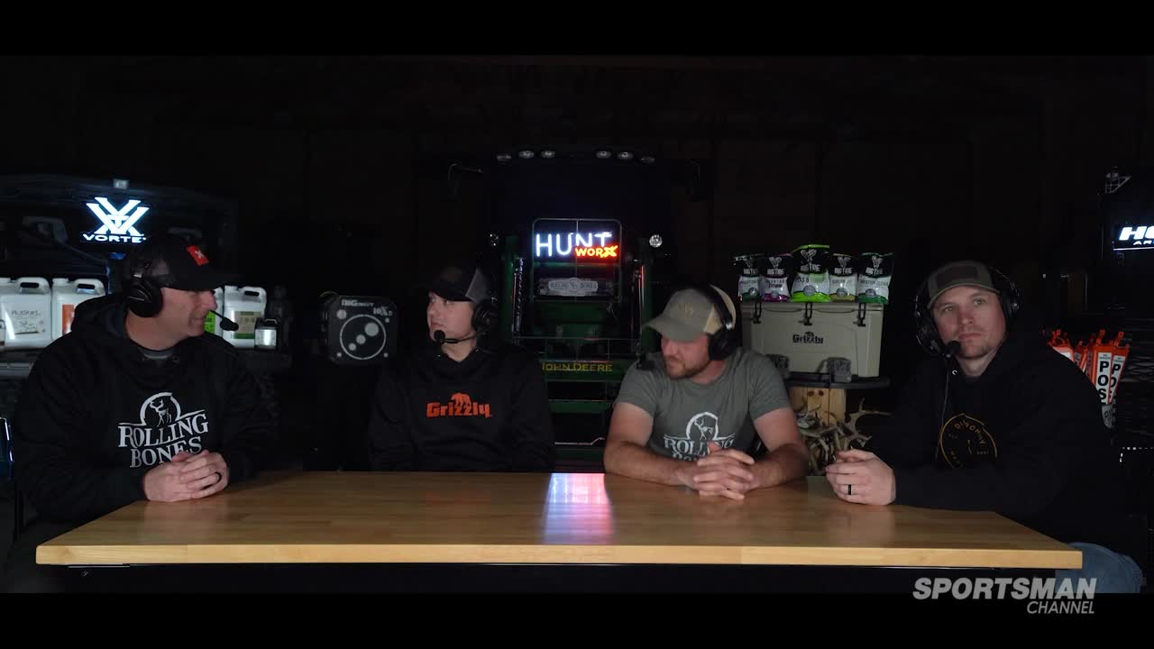 Four men sit at a table, each wearing a headset microphone. The "Sportsman Channel" logo is visible, and a neon sign reads "Hunt Work" in the background.
