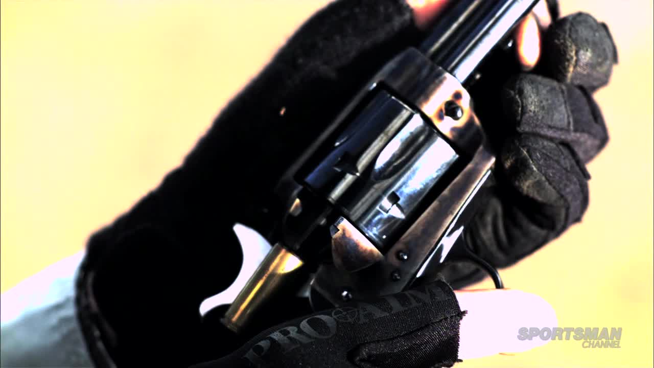 A black-gloved hand holds a revolver, the barrel pointed away. The Sportsman Channel logo is visible in the corner.
