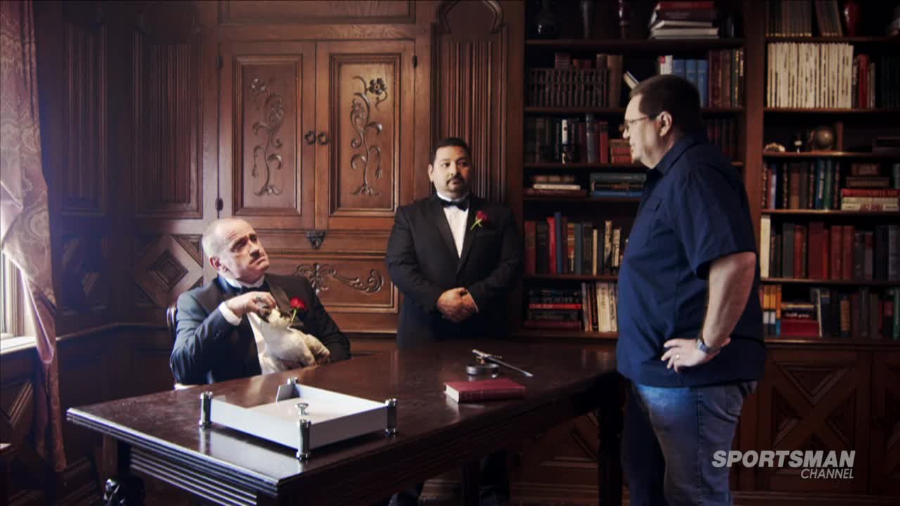 A man in a tuxedo stands between two others, one holding a stuffed animal and the other in a blue shirt. The scene is set in a wood-paneled room, with a Sportsman Channel logo visible.

