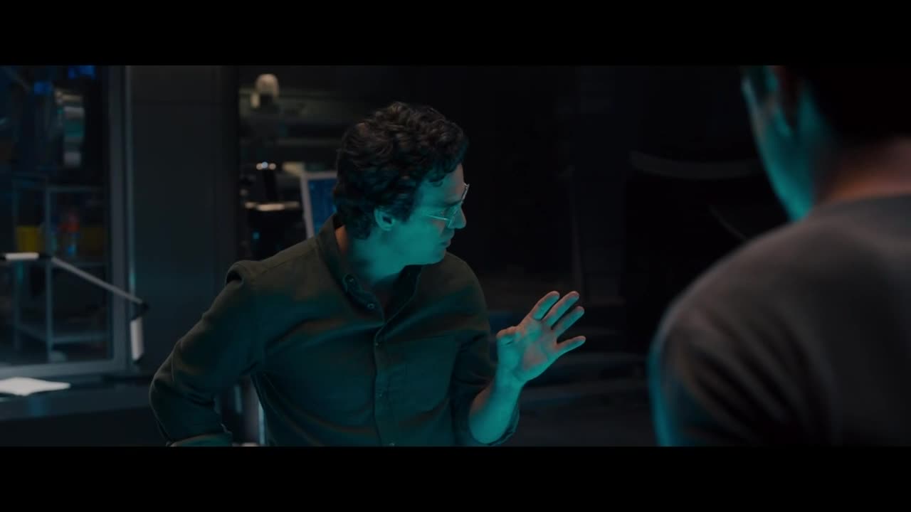 The man in glasses gestures with his right hand, fingers spread wide, as he speaks. His gaze is fixed on the person facing him, who is mostly out of frame.
