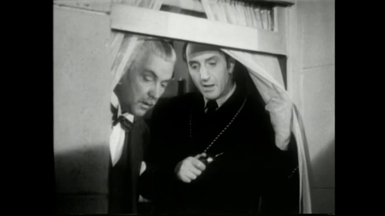 Two men, both in dark suits, are peering from behind a curtain, one holding a pocket watch. The man on the right is speaking, his eyes focused on the watch in his hand.
