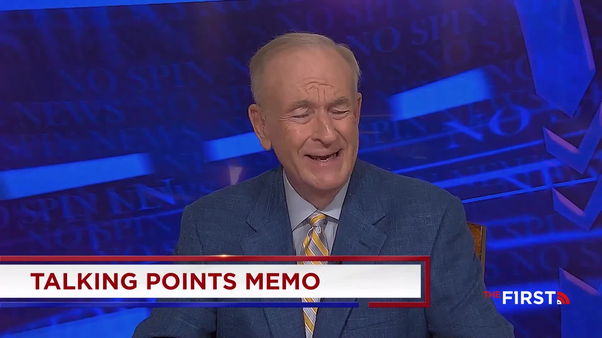 A man in a blue suit and yellow tie grins widely, speaking on a set for The First TV. Below him, a banner reads "Talking Points Memo."
