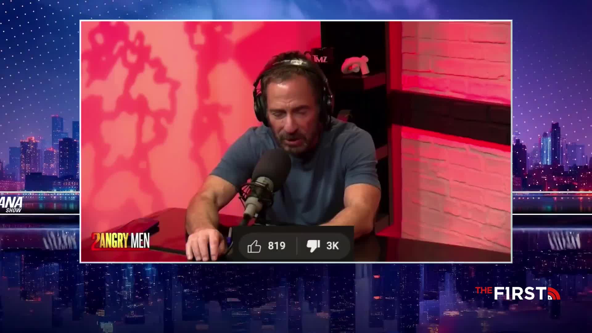 A man wearing headphones sits at a microphone, looking down with a somber expression. The "2 Angry Men" logo appears in the corner of the screen, while the background shows a city skyline on "The First" TV broadcast.
