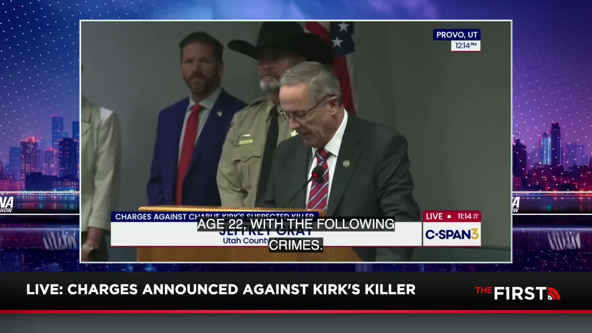 A man in a suit and tie reads from a podium, his voice amplified on C-SPAN3. Behind him, other men stand at attention, the backdrop a simple wall under the American flag.
