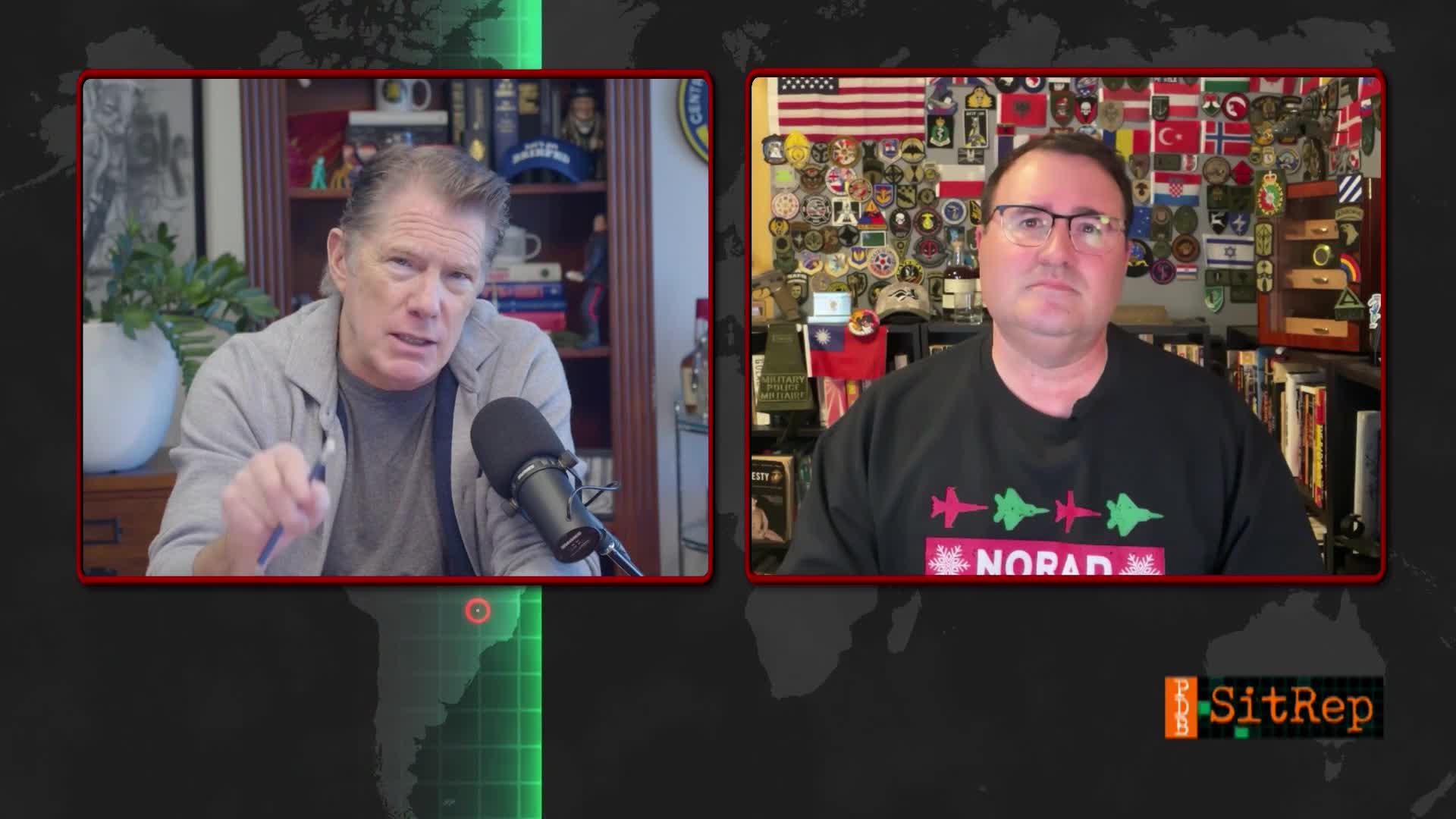 Two men are on a split screen, discussing something on a United States TV show. The man on the left gestures with a pen, while the other sits calmly, surrounded by flags and military patches.
