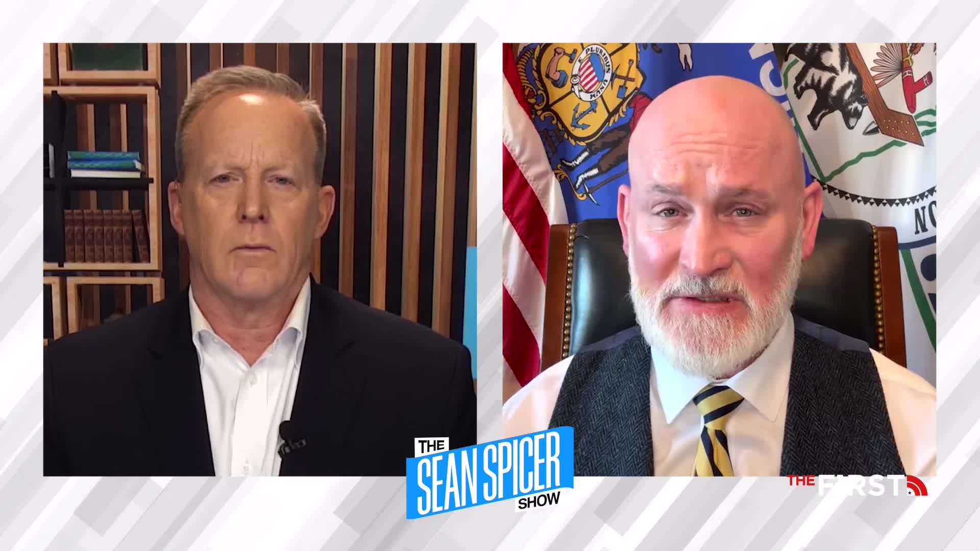 Two men are on screen, likely on "The Sean Spicer Show" on The First TV, with one speaking while the other listens intently. The man on the right is in front of a flag, and the other is in a studio setting.
Two men are on screen, likely on "The Sean Spicer Show" on The First TV, with one speaking while the other listens intently. The man on the right is in front of a flag, and the other is in a studio setting.