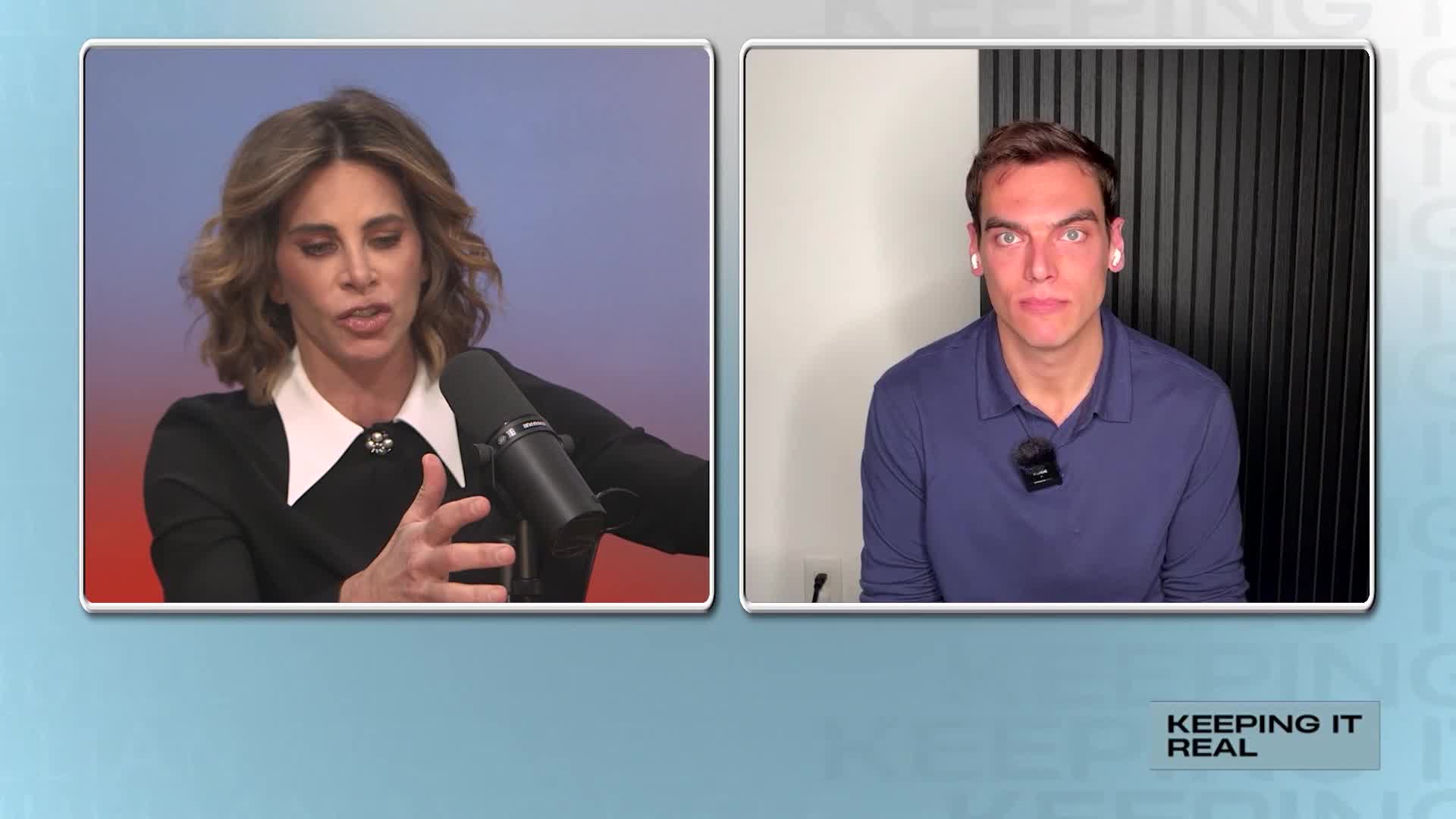 A woman with blonde hair, wearing a black jacket with a white collar, gestures with her hands while speaking into a microphone. Beside her, a man in a blue shirt looks directly at the camera with a serious expression.