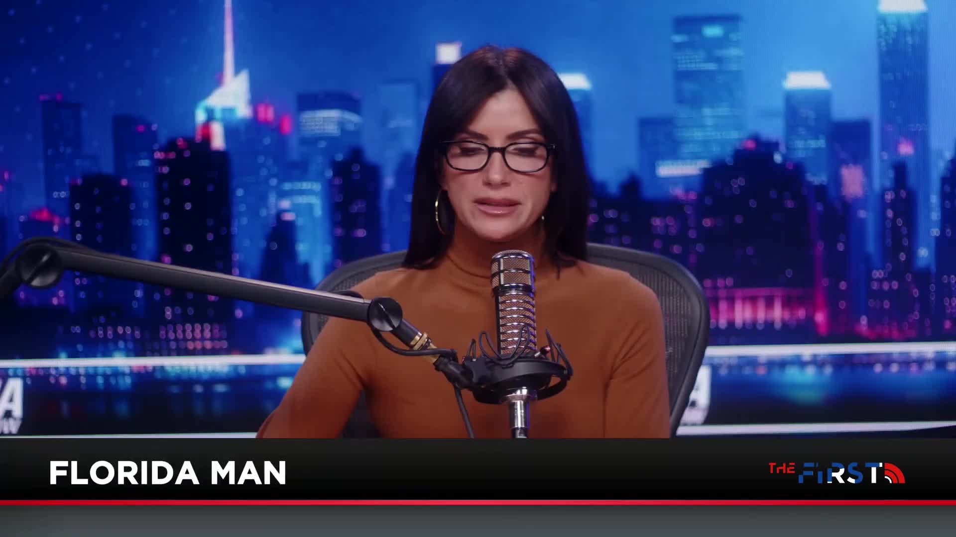 A woman with dark hair and glasses speaks into a microphone, seated before a backdrop of a city skyline at night. A graphic at the bottom of the screen reads "FLORIDA MAN" and "THE FIRST."
