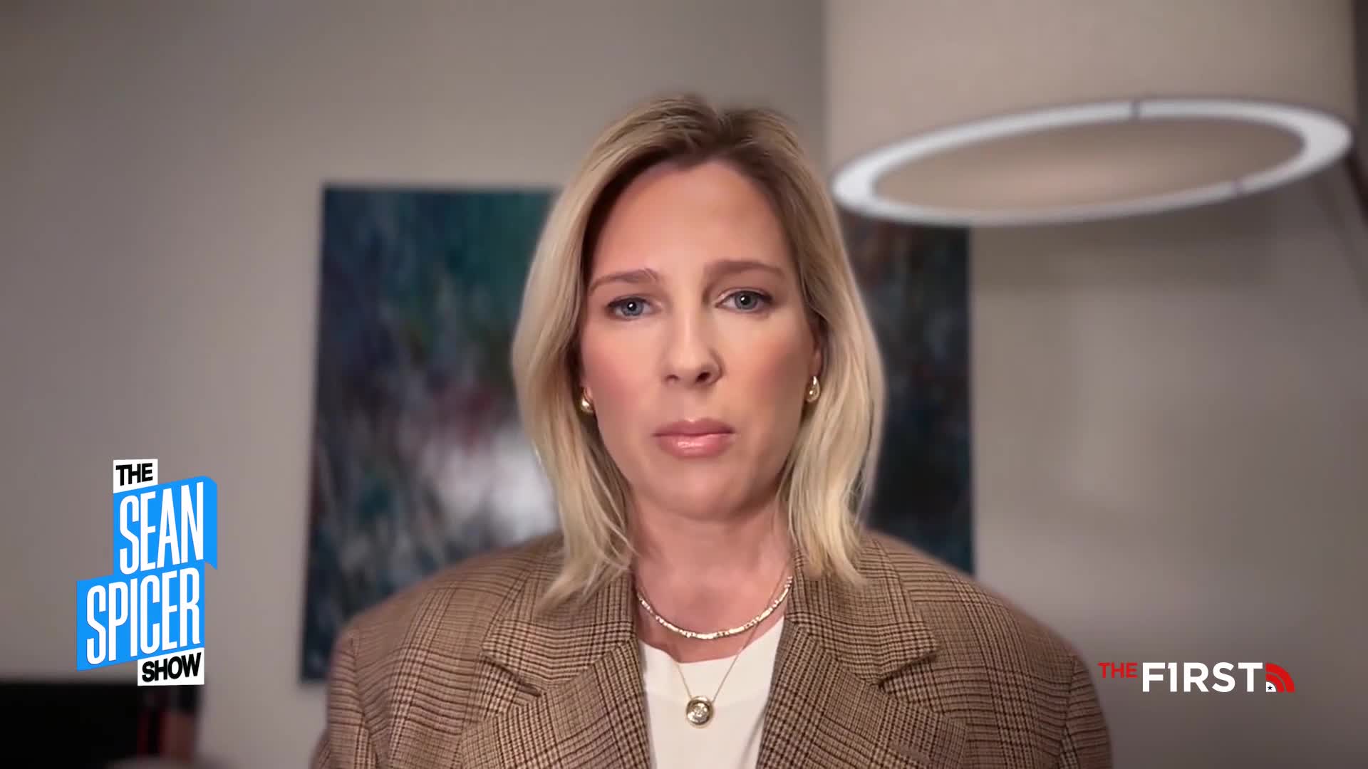 A woman with blonde hair and a plaid jacket looks directly ahead. A logo for "The Sean Spicer Show" appears on the left, and "THE FIRST" is visible on the right.