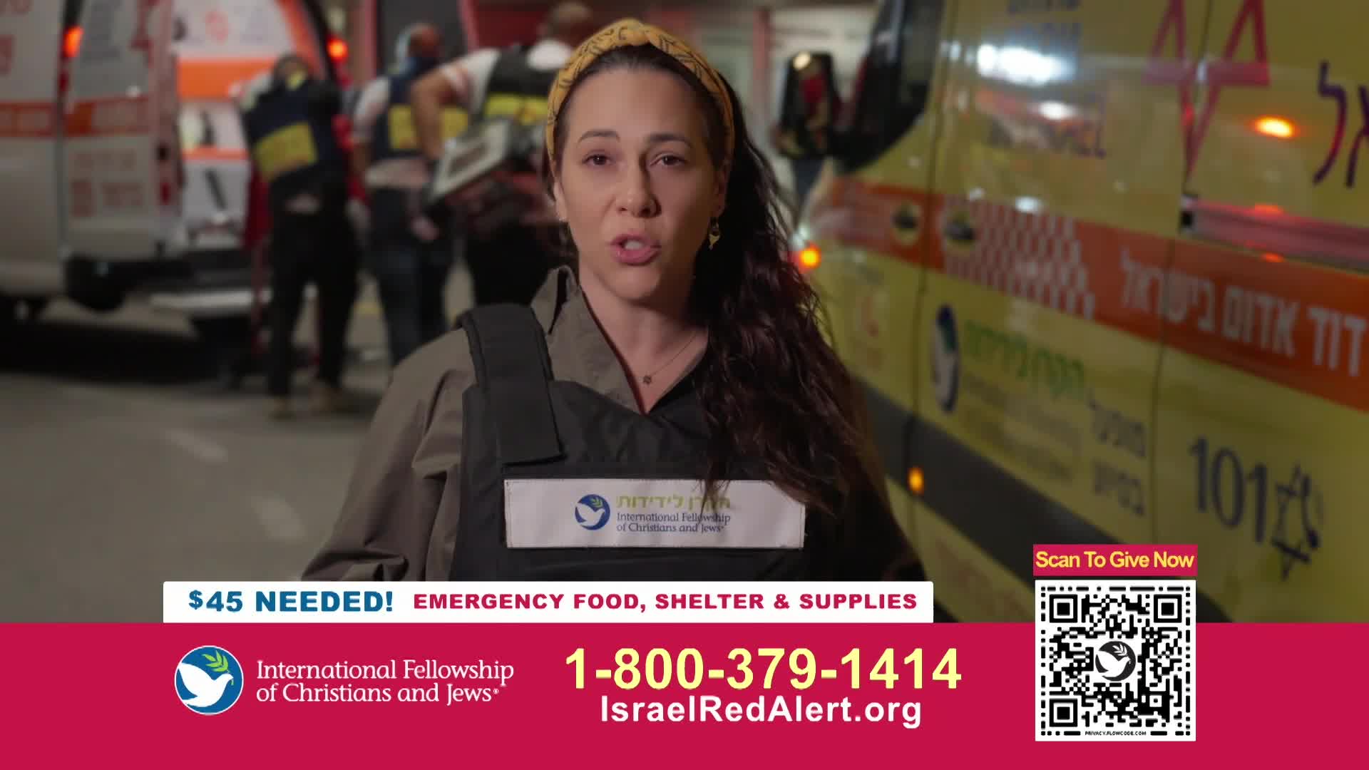 A woman in a vest speaks directly to the camera, with ambulances and emergency personnel behind her. The scene is illuminated by flashing lights and the glow of streetlights.