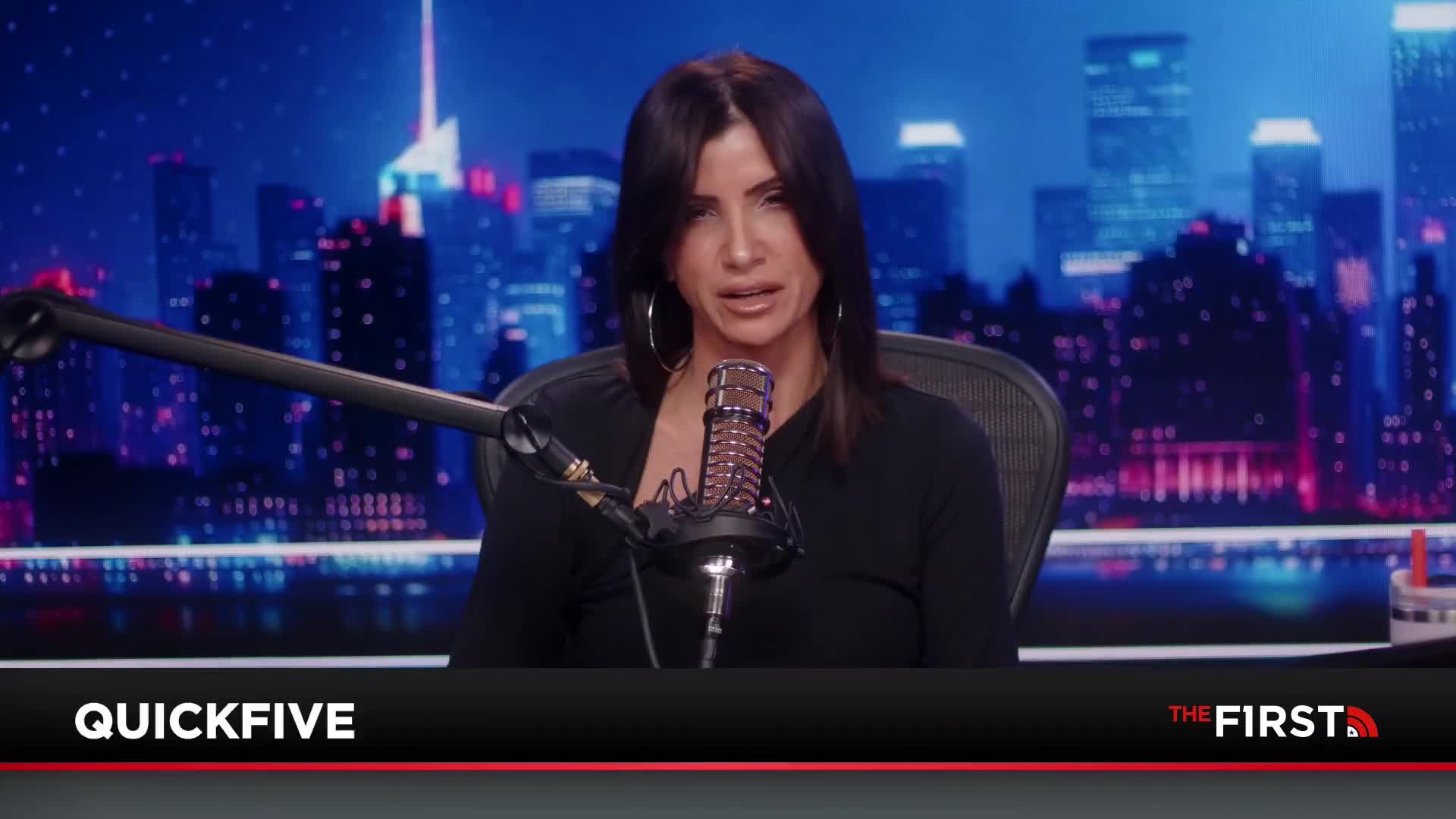 A woman with dark hair and hoop earrings speaks into a microphone. Behind her, a cityscape glows with neon lights.