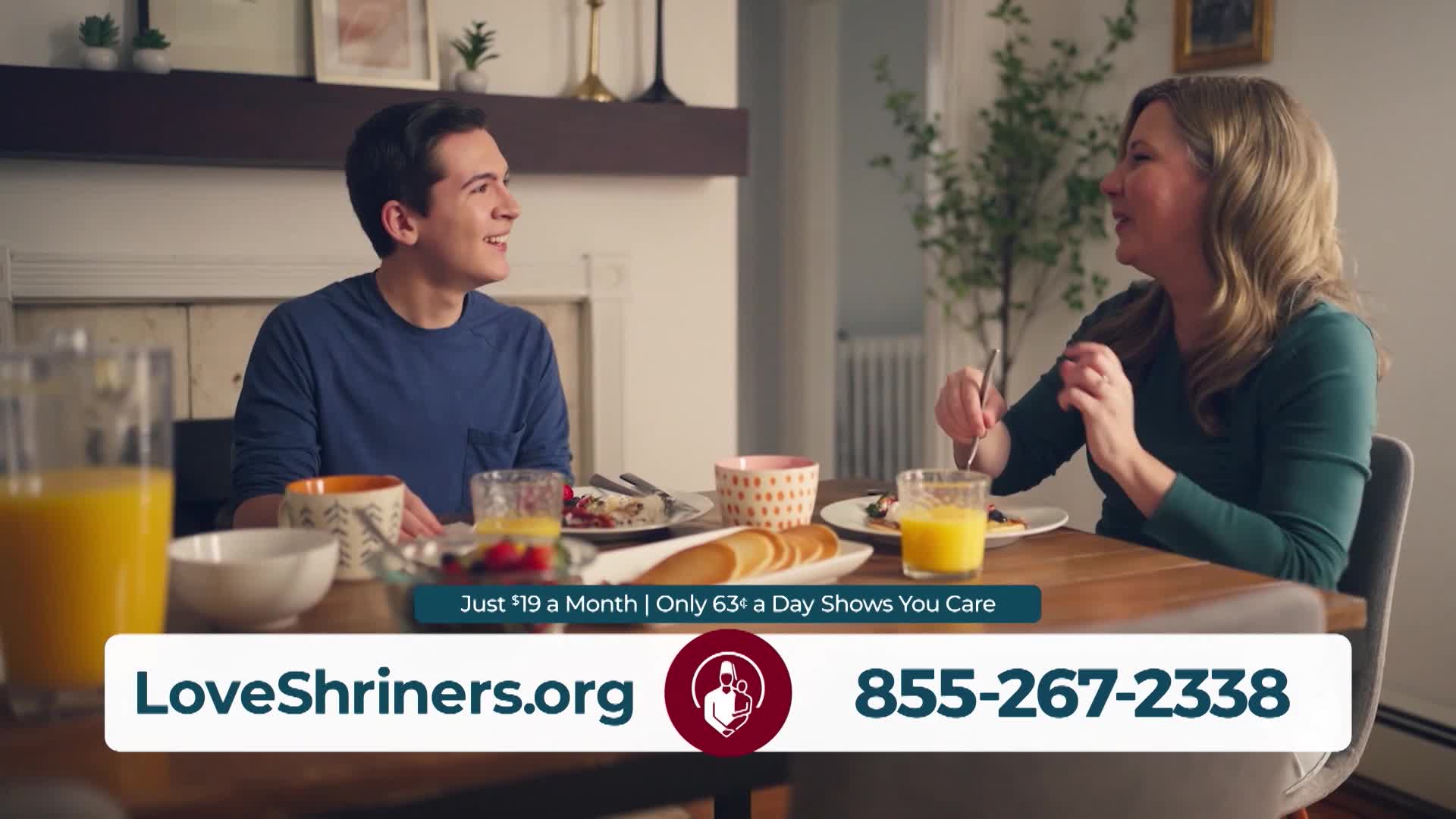 A young man and woman sit at a table, sharing a meal and conversation. A glass of orange juice sits on the table, along with plates of food.