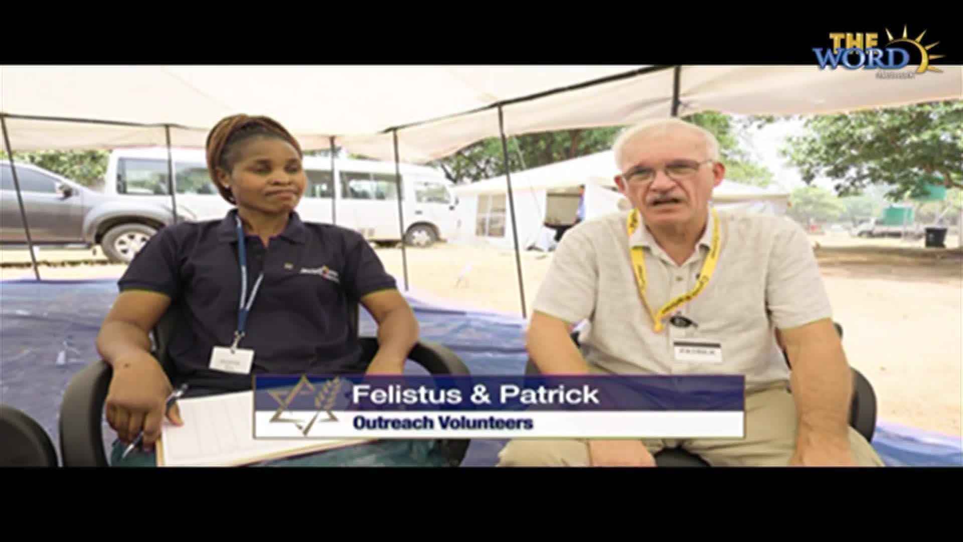 Under a white canopy, two people, Felistus and Patrick, sit in chairs. A graphic on the screen from The Word Network identifies them as outreach volunteers.
