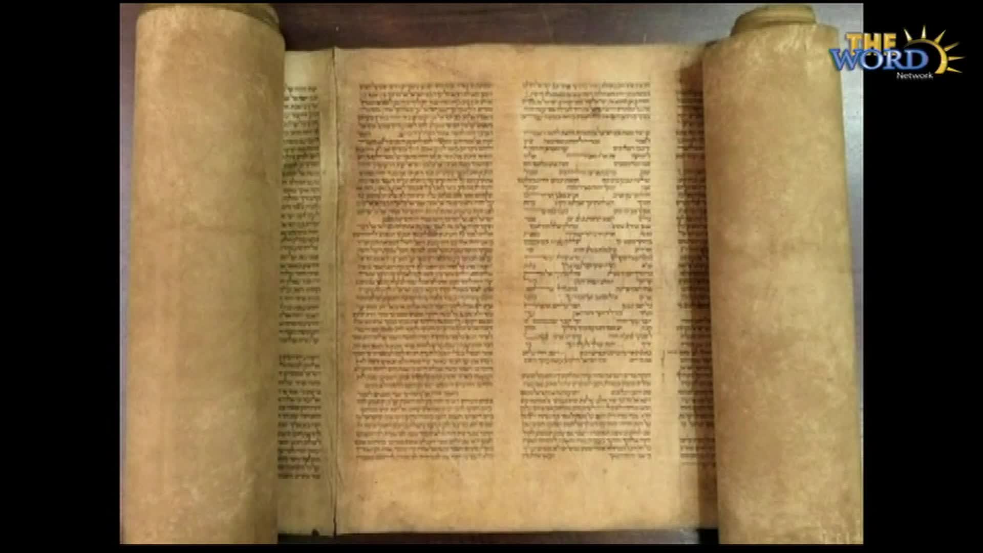 A parchment scroll, unrolled, displays tight columns of Hebrew script. The Word Network logo is visible in the corner, suggesting a broadcast about this ancient text.
