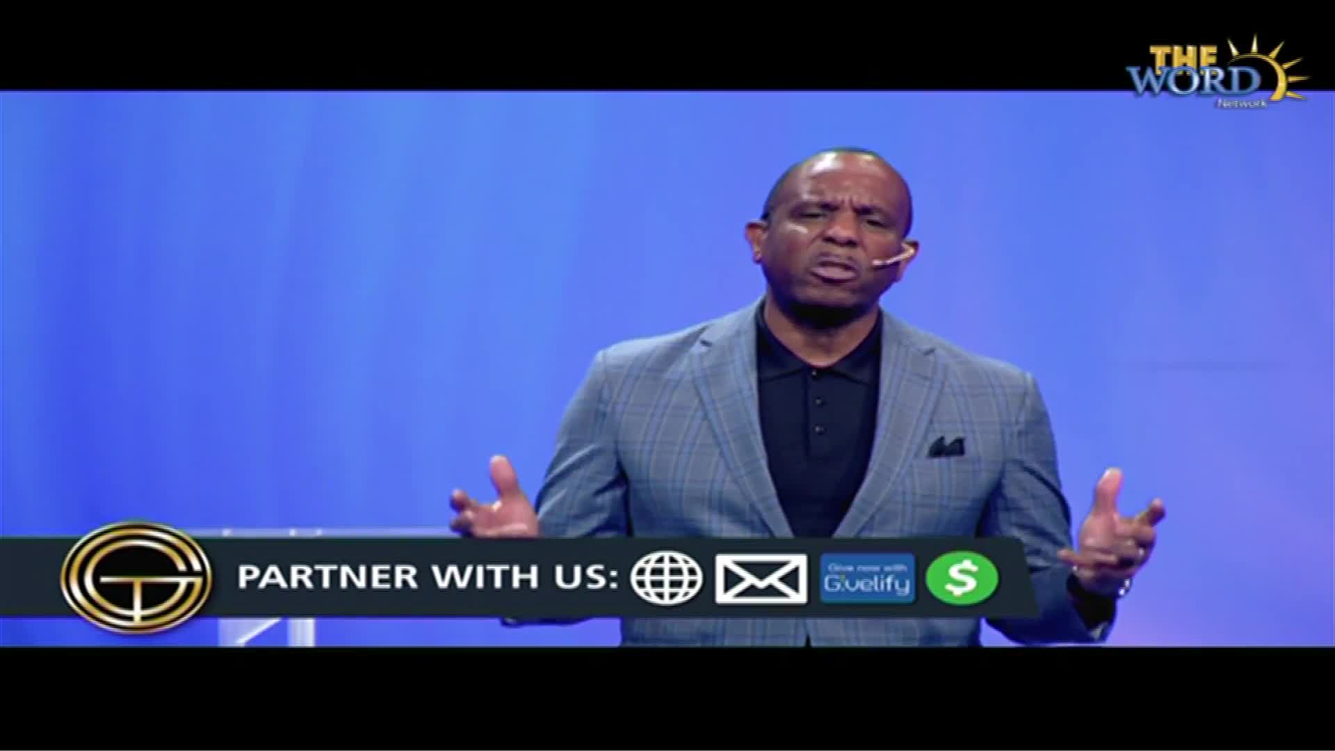 A man in a blazer, speaking into a headset microphone, gestures with his hands as he addresses the camera. Below, a graphic on The Word Network encourages viewers to partner with them.
