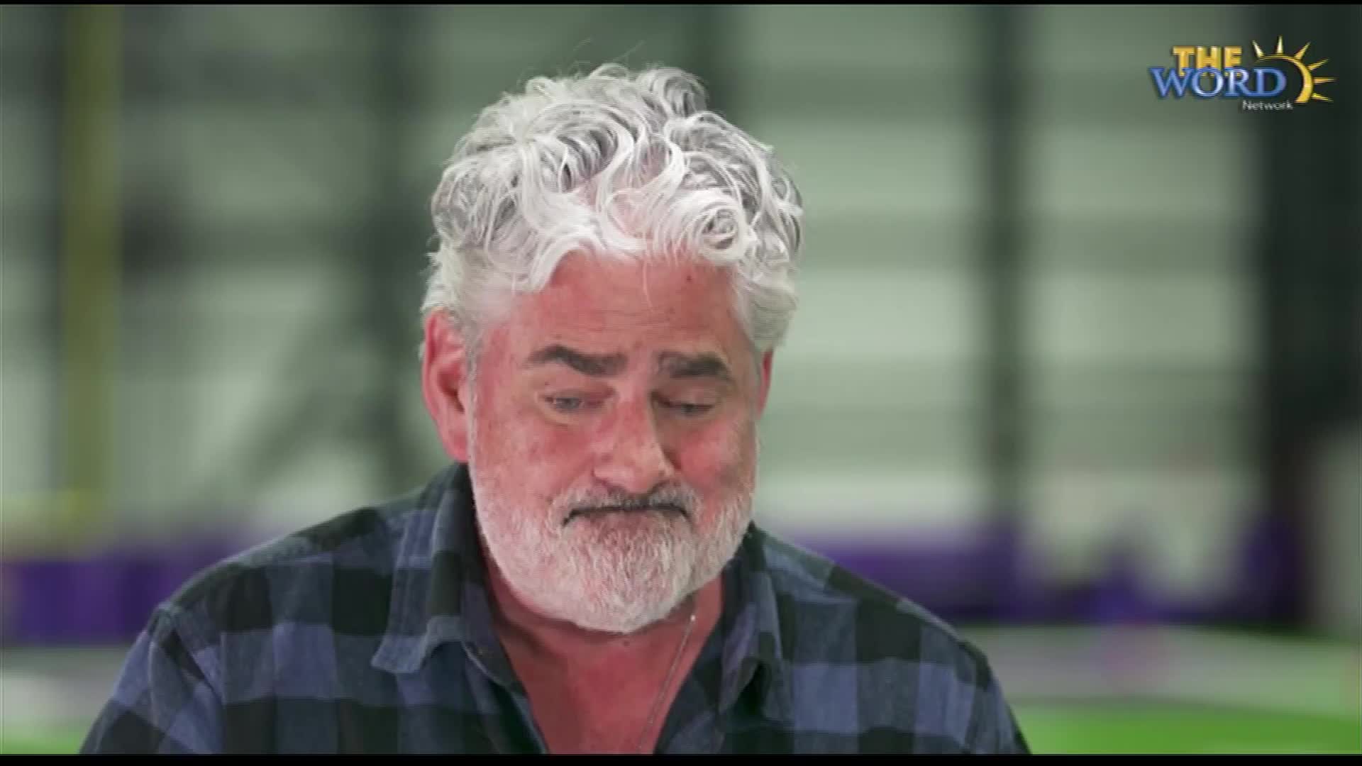 The man with the silver hair and beard is looking down, his expression thoughtful. He's wearing a plaid shirt, and the logo for The Word Network is visible in the corner.

