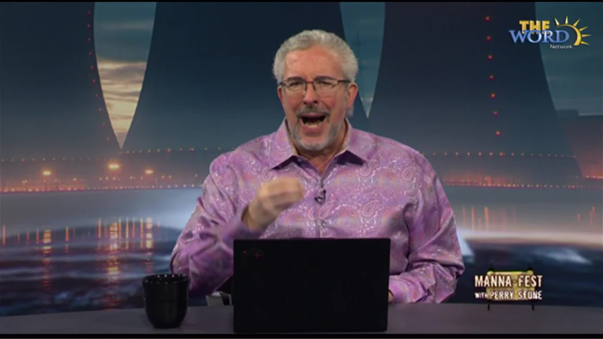 A man in a paisley shirt gestures emphatically while speaking, his mouth wide open. Behind him, a backdrop of a cityscape glows under a dark sky, with The Word Network's logo visible.
