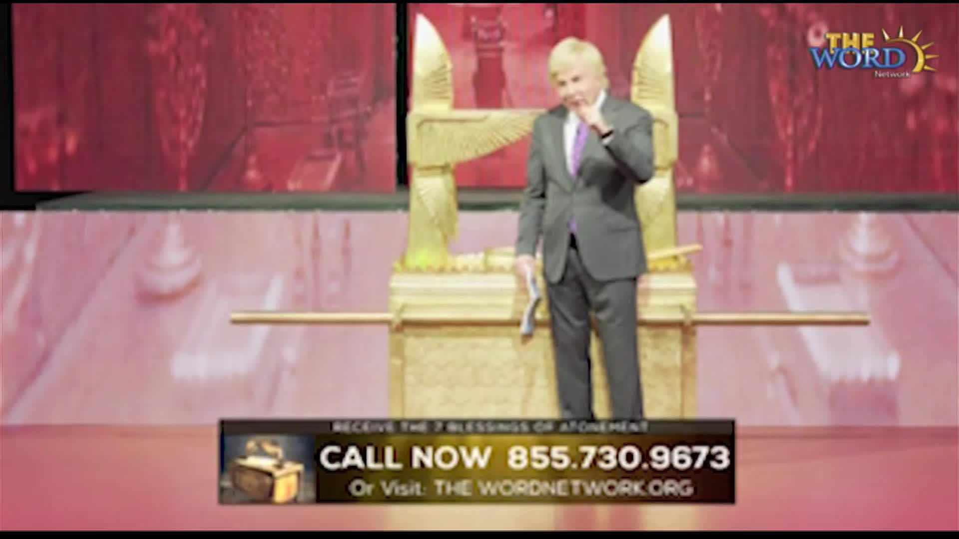 A man in a suit stands on a stage in front of a golden structure, holding a small paper. He touches his face thoughtfully, while a call-to-action banner sits at the bottom of the screen.
