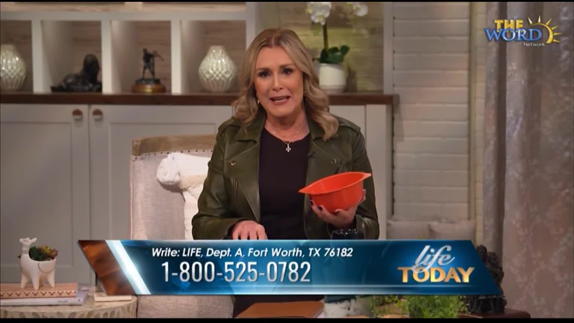 A woman, seated in a studio, holds a small orange bowl. The screen displays contact information for "Life Today" on The Word Network.
