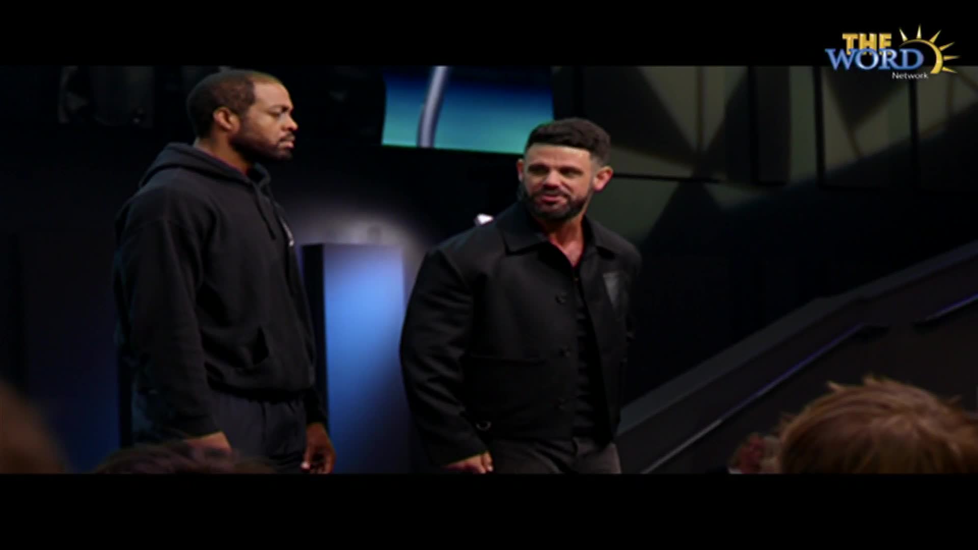 Two men stand on a stage, the one on the right in a black jacket and the other in a black hoodie. The Word Network logo is visible in the top right corner.
