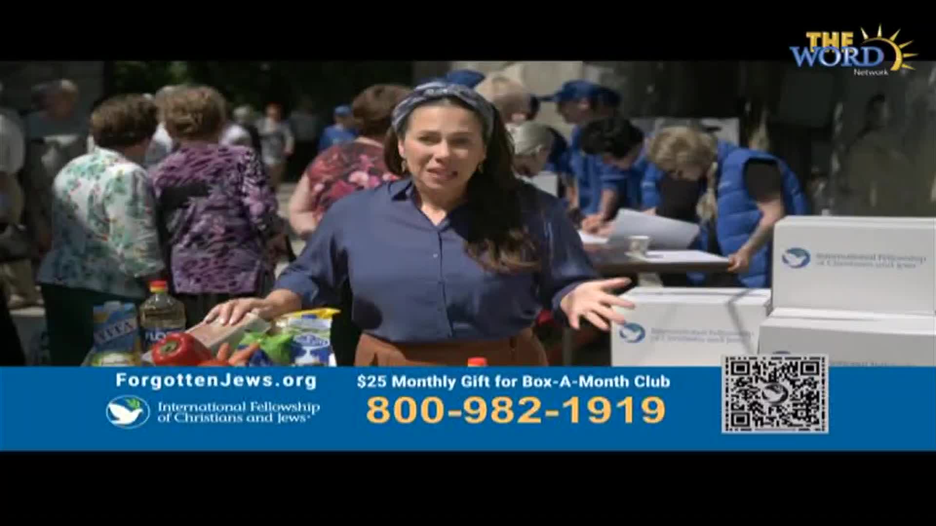 A woman in a blue shirt gestures towards a table laden with groceries. Behind her, people in blue vests are writing at a table, likely in the United States, as part of a broadcast on The Word Network.
